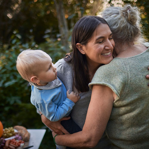 happy woman holding a baby boy and hugging an older woman
