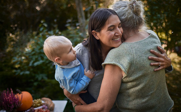 happy woman holding a baby boy and hugging an older woman