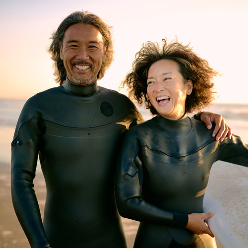 happy couple in wetsuits on the beach