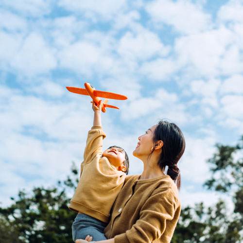 mother holding child playing with toy plane