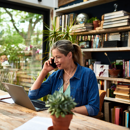 woman talking on mobile phone and looking at laptop at home